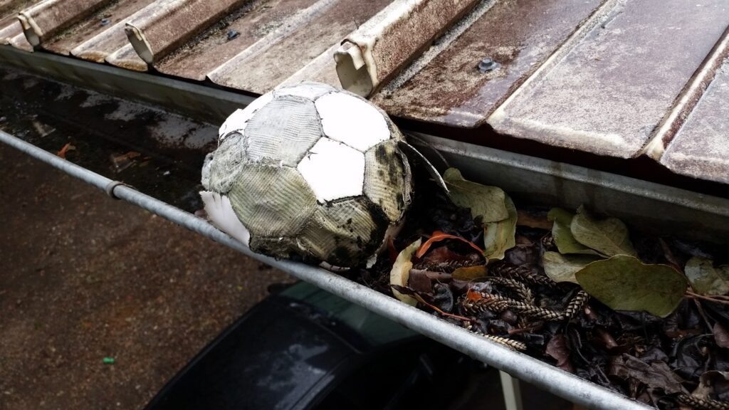 gutter cleaning, old soccer ball and leaves in roof gutter